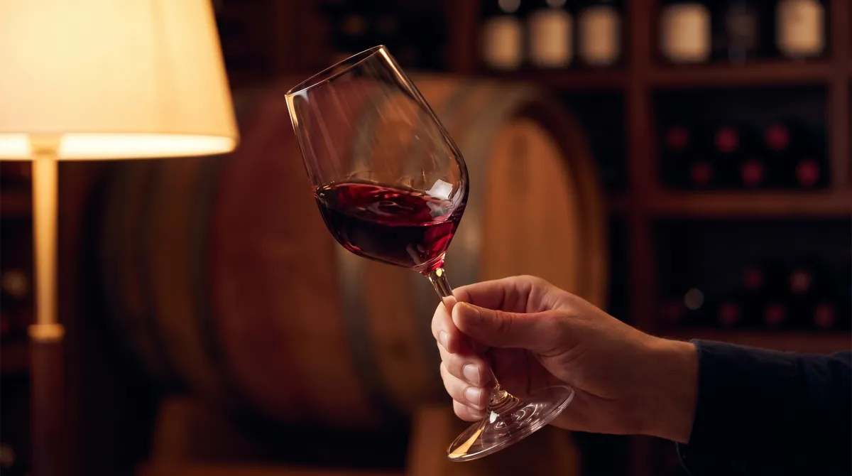 A hand swirling a glass of red wine in a softly lit wine cellar